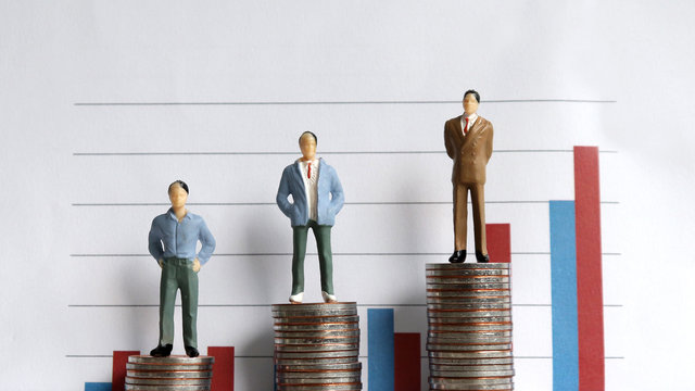 Miniature people standing on a pile of coins in front of a graph. The concept of the gap between the rich and the poor in society.