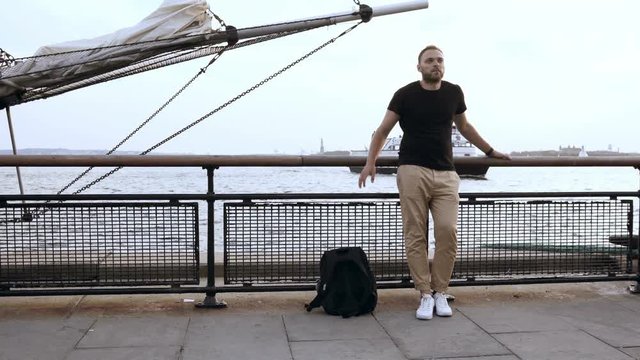 Young handsome man with backpack standing on the pier near the bowsprit, motor boat is coming to the shore.