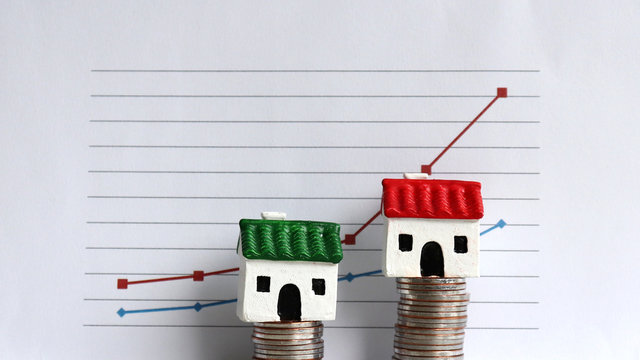 Housing price rising and differentiated concept. A Miniature House On A Pile Of Coins In Front Of A Graph.