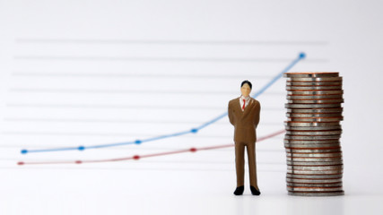 A pile of miniature man and coins stands in front of a linear graph.
