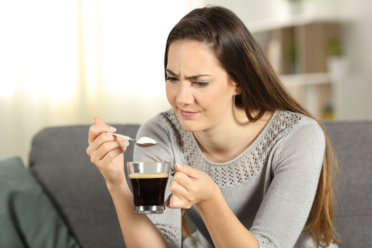 Doubtful woman throwing sugar into coffee