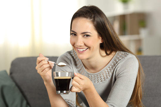 Happy woman throwing sugar into coffee looking at you