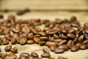 Coffee beans spilled onto a wood table with the focus on the beans near the viewer.