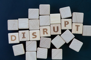 Business disruption, evolve or game changer concept, straggle cube wooden blocks with some combine the word DISRUPT on dark black chalkboard background