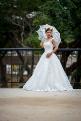 Young girl in a bridal gown holding a white umbrella on a steel bridge.