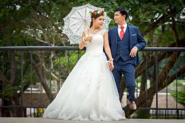 Couple standing holding hands while bride holding white umbrella.