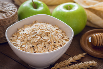 Oat flakes in white bowl with fresh green apple and honey