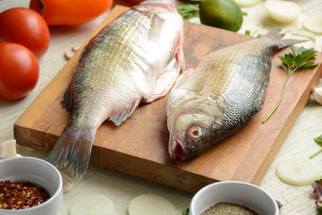 Fresh uncooked dorado or sea bream fish with lime, herbs,  vegetables and spices on rustic  wooden board over white backdrop, top view.   Healthy food or diet nutrition concept. 