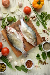 Fresh uncooked dorado or sea bream fish with lime, herbs,  vegetables and spices on rustic  wooden board over white backdrop, top view.   Healthy food or diet nutrition concept. 