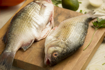 Fresh uncooked dorado or sea bream fish with lime, herbs,  vegetables and spices on rustic  wooden board over white backdrop, top view.   Healthy food or diet nutrition concept. 