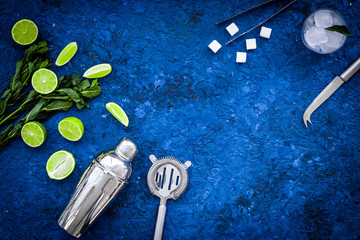 Ingredients and crockery for making mojito. Slices of lime, mint, sugar cubes, glass with ice cubes, shaker, strainer on blue background top view copy space