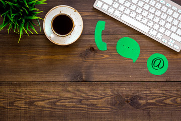 Customer service concept. Concact information. Phone, message, email signs on office work desk with computer on dark wooden background top view copy space