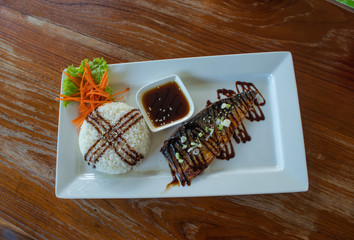 Rice and grilled saba sauce on a white plate on a wooden table.