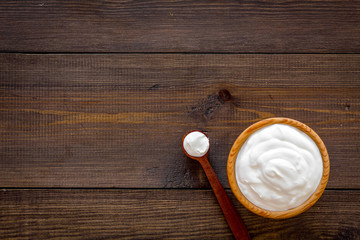 Healthy product, healthy meal. Greek yogurt in brown bowl near spoon on dark wooden background top view copy space