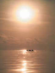 Sun over horizontal line and water with a littelboat, idyllic secenery.