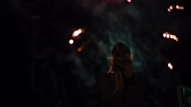 Back view of standing woman looking and filming fireworks on smartphone