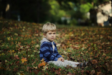 Little boy, playing in the rain in autumn park, leaves around him