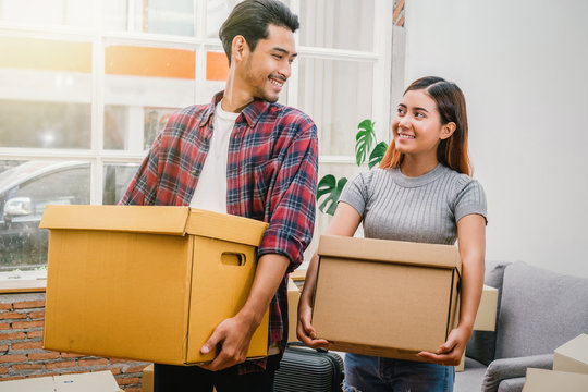 Asian young couple carrying big cardboard box for moving in new house, Moving and House Hunting concept