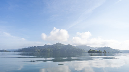 Beautiful high mountains and clear water at Cheow Lan Lake in Khao Sok National Park with morning light, reflection of blue sky and clouds on the sea.