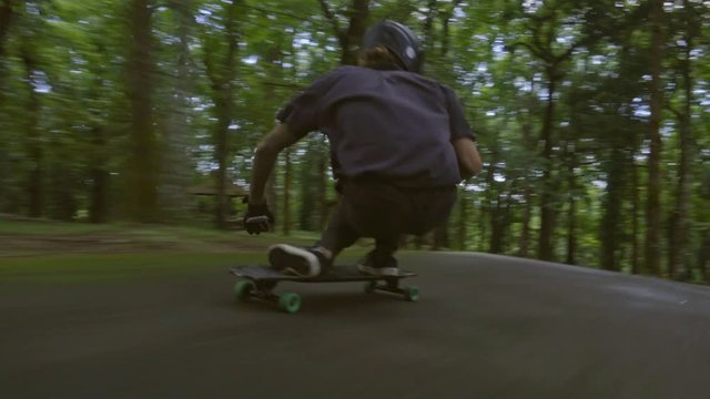 Follow low angle shot of young man in helmet moving on his skateboard, leaning forward and then sitting down