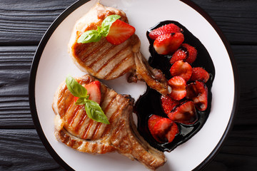 grilled pork steak with a bone with balsamic strawberries close-up on a plate. Horizontal top view