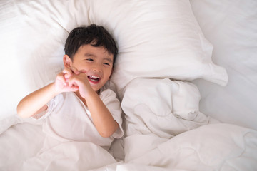 3 years old little cute Asian boy at home on the bed, kid lying playing and smiling on white bed...