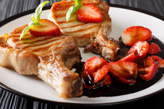 grilled pork steak with a bone with balsamic strawberries close-up on a plate on a table. horizontal