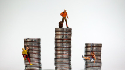 Miniature people climbing up a pile of coins with ropes. Income difference and employment gap...