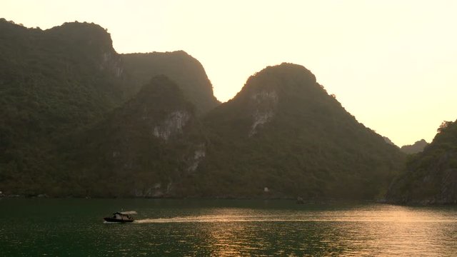 Traditional fishing boat sailing at sunset through the limestone islands in UNESCO World Heritage site, Ha Long Bay, Cat Ba National Park, Vietnam