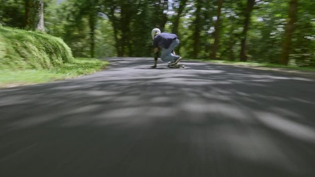 Man in helmet riding his skateboard on warm summer day, camera is behind him and then moves forward before him
