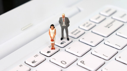 A miniature man and a miniature woman standing on a different volume keyboard. The concept of...