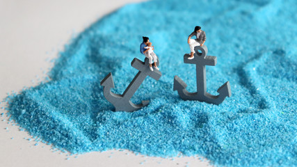 Two gray anchors on the blue sand with two miniature women holding a baby. The concept of fixed...