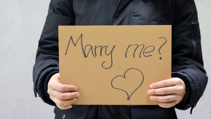 A woman holds a paper with the inscription “Marry me?