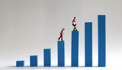 Two miniature people walking on a blue bar graph. Economic income gap concept.