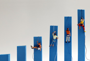 Miniature people climbing on hand blue bar graphs. The concept of competition for success.