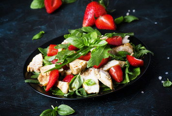 Grilled chicken salad, fresh strawberries and spicy arugula, dark background, selective focus