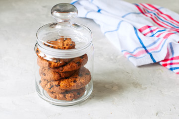 Stack of  homemade chocolate chip cookies in glass jar. White stone background.
