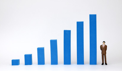 A miniature man in formal clothes next to blue bar graph.