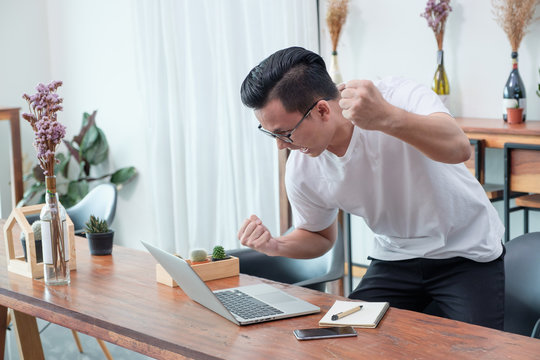 Asian Casual Man Standing And Arm Up Celebrate Good New From Mobile At Laptop In Coffee Shop,success Business Concept,work Outside Office,work At Home.