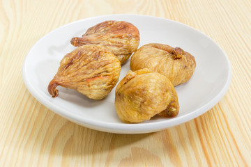 Dried figs on the white saucer on a wooden surface