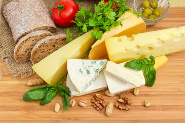 Several pieces of different cheese among of bread, vegetables, greens