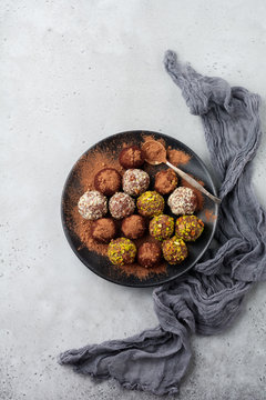 Variety of homemade dark chocolate truffles with cocoa powder, pistachios, almonds in light gray background texture. Top view, copy space.