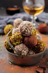 Variety of homemade dark chocolate truffles with cocoa powder, pistachios, almonds in dark brown background texture. Top view, copy space.