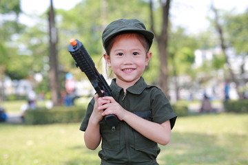 Little Asian child girl in pilot soldier suit costume with holding gun in hands at the garden.