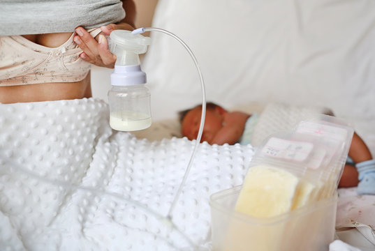 Close-up mother using automatic breast pump on the bed.