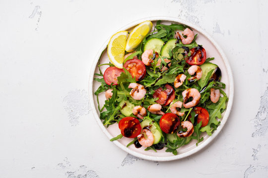 Arugula, cucumber, tomato and shrimp salad with soy sauce on a ceramic plate. Selective focus. Top view.