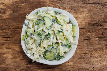 Spring salad with cabbage, cucumber, green onion, parsley and mayonnaise on wooden table