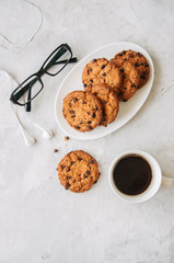 Chocolate chip cookies  in a white plate cup of coffee  eyeglasses and headset  on a white stone background. Top view and copy space.