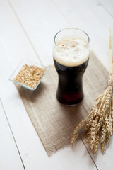 glass of dark beer with wheat on a wooden table background