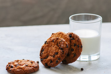 Homemade chocolate chip cookies and glass of fresh milk on a white stone background.
